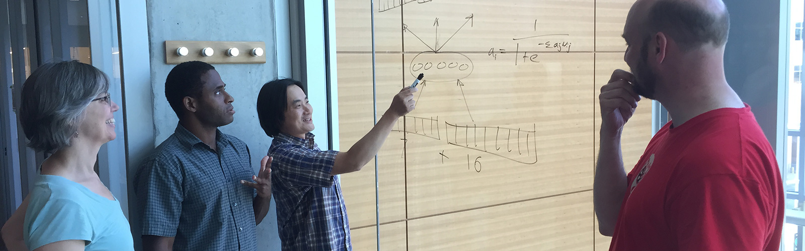 Researchers collaborate, aided by a diagram drawn on a window.