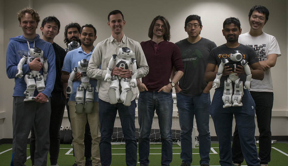 Josiah Hanna and team stand holding robots as if they're puppies.